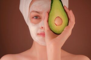 A close-up of a person applying moisturizer to their face, surrounded by natural skincare products and plants.